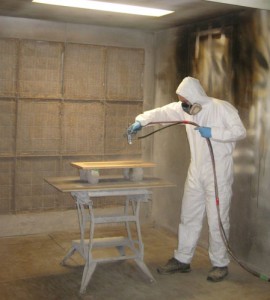 Craig in a dry suit spraying a wood panel